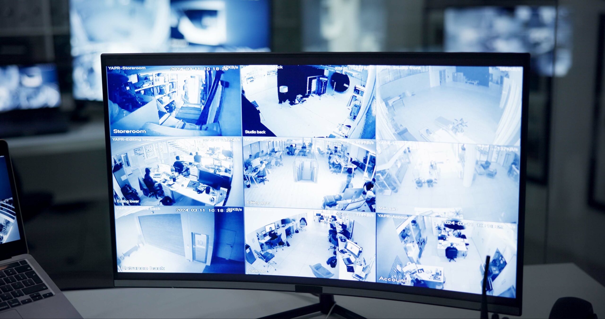 black monitor showcasing live security camera footage broken into 9 grids with more monitors in the background